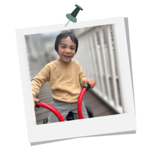 little boy in a tan sweatshirt rides a red tricycle on a ramp